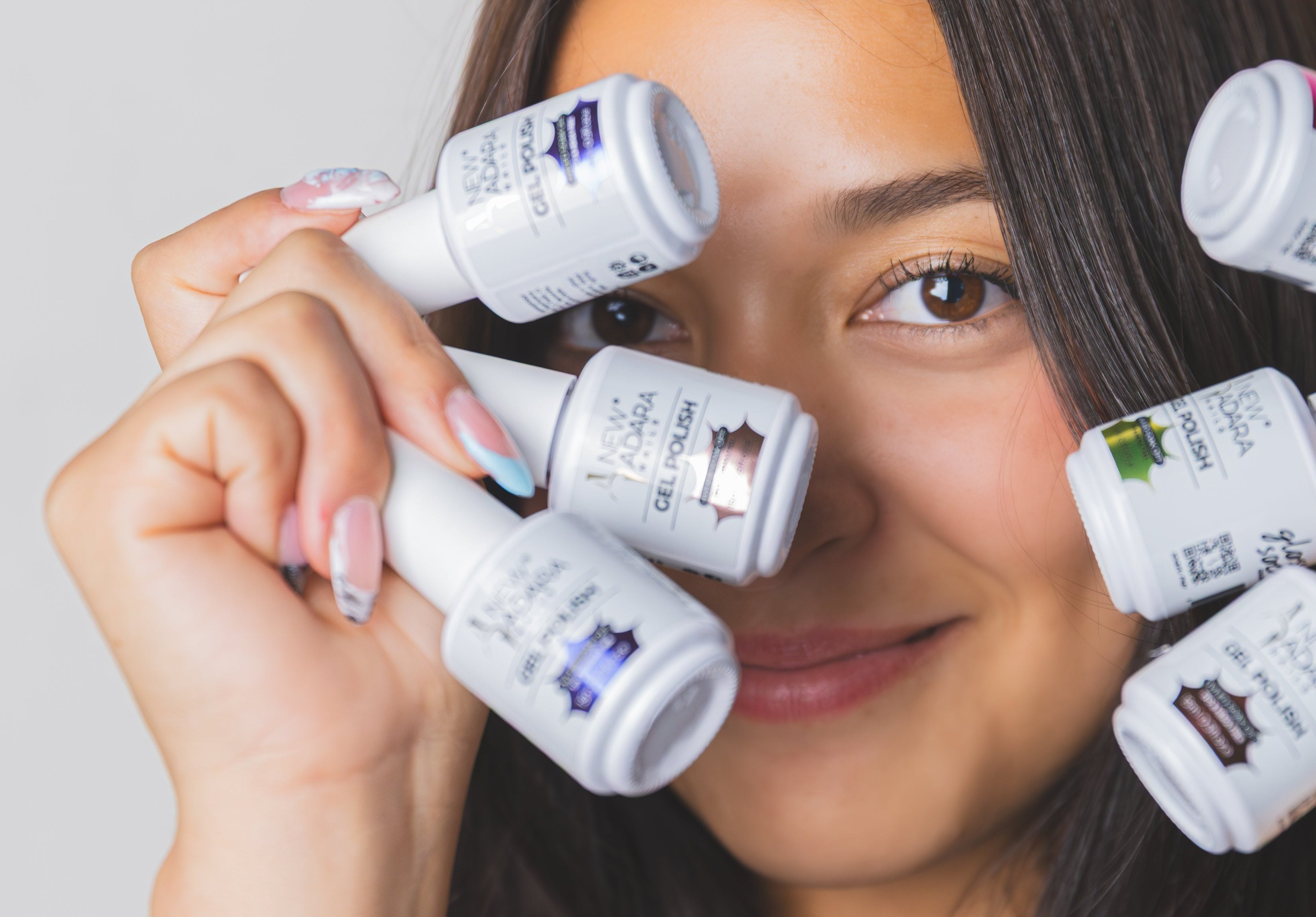 A woman holding New Adara gel polish bottles in front of her face